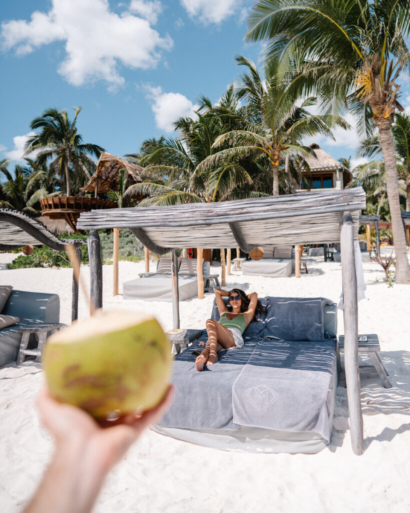 adriana maria laying on beach cabana under palm trees on tulum beach mexico