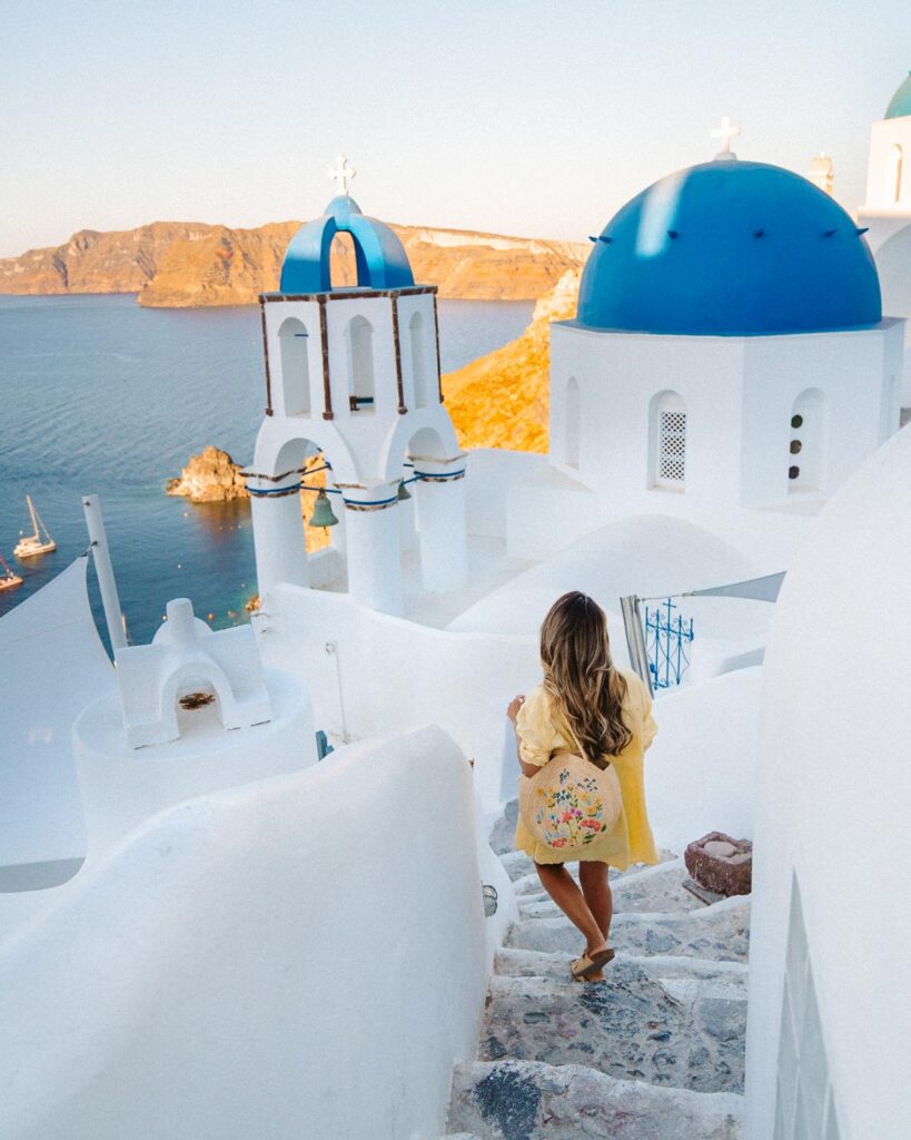 Best Santorini photo spots, girl walking down stairs with Santorini blue domes,
