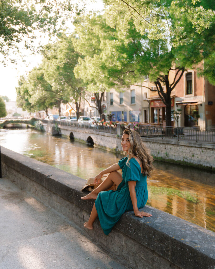 girl sitting on edge of canal in summer in L’Isle sur la Sorgue, provence france

