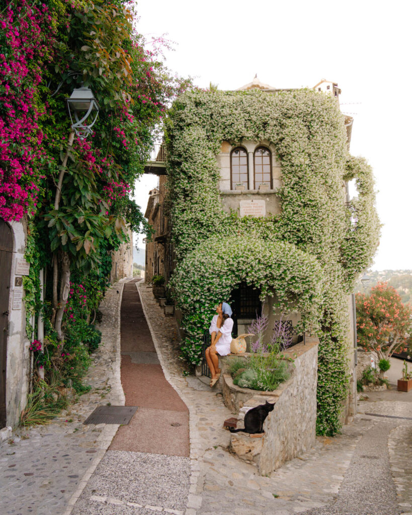 Adriana Maria sitting in front of traditional village house covered in jasmine flowers  in Saint Paul de Vence