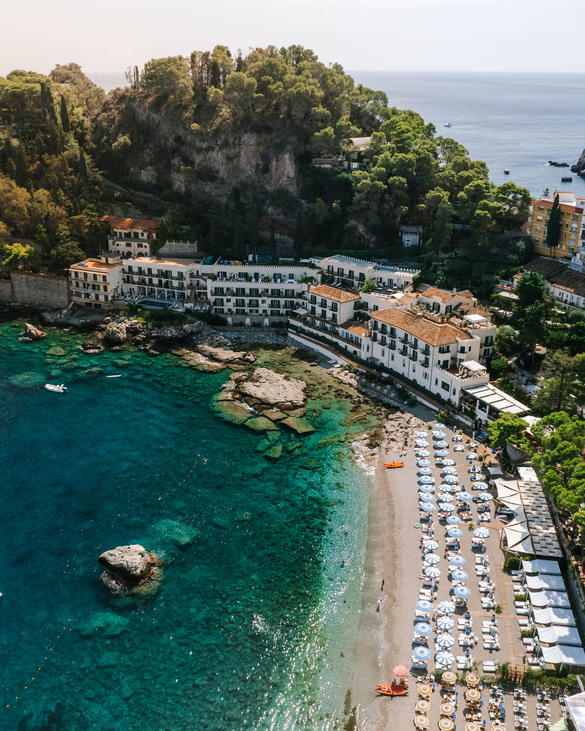 Aerial view of Taormina’s coastline with clear blue water and greenery.