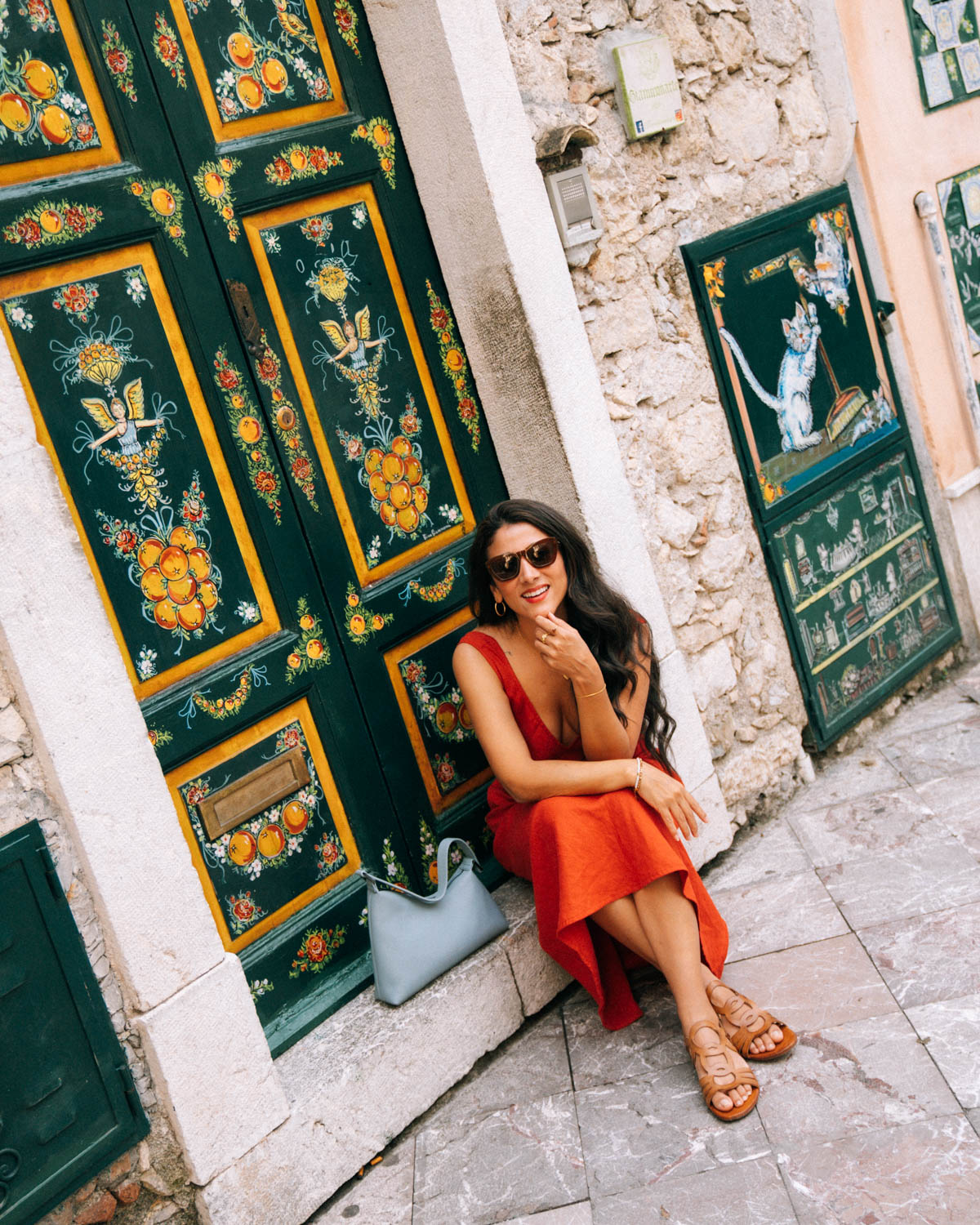 Woman in a red dress by a painted Sicilian door in Taormina, one of the best places to visit in Sicily
