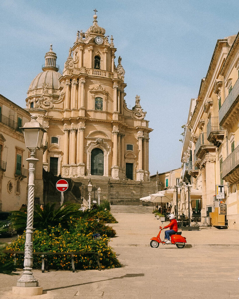 a red vespa drives through the streets on ragusa sicily