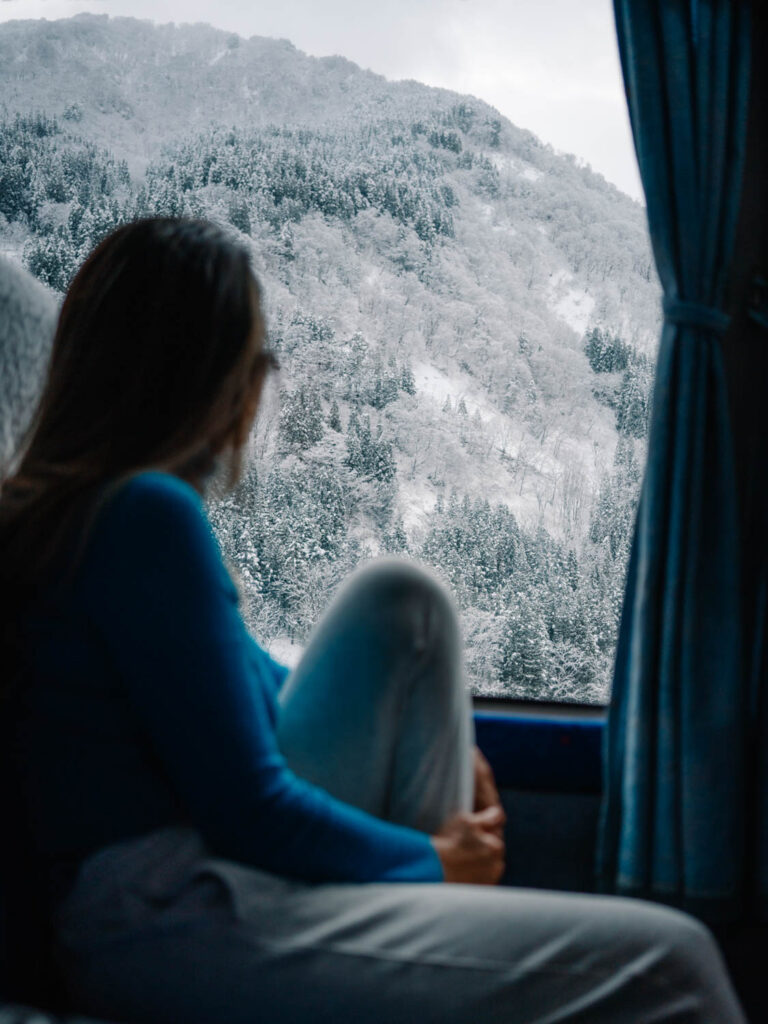 a woman looks out the window of a bus to a snowy alpine scene in japan